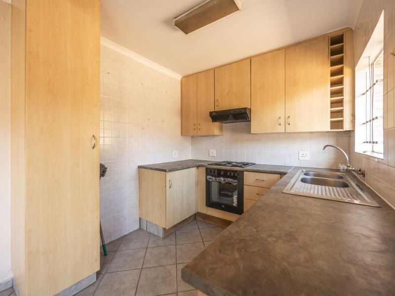 A functional kitchen featuring light wood cabinetry, laminate countertops, a built-in oven with hob, and a double bowl stainless steel sink.