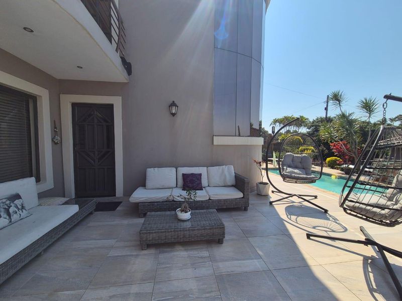 A spacious covered patio area featuring tiled flooring and recessed lighting, providing direct access to the swimming pool and garden area.