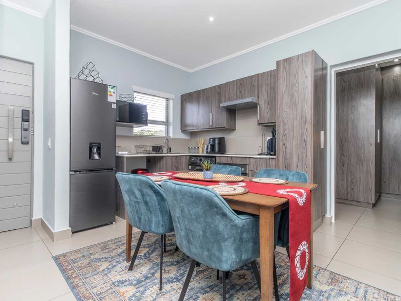 Modern open-plan kitchen and dining area featuring contemporary wood-grain cabinetry, tiled flooring, and integrated storage solutions in a well-maintained apartment setting.