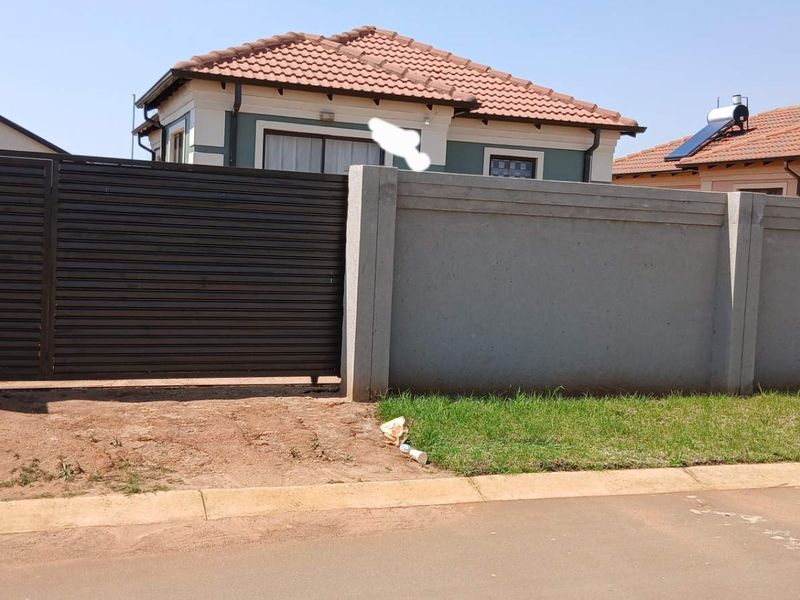 Front view of the property featuring a secure perimeter wall, sliding gate, and tiled roof structure with solar water heating system.