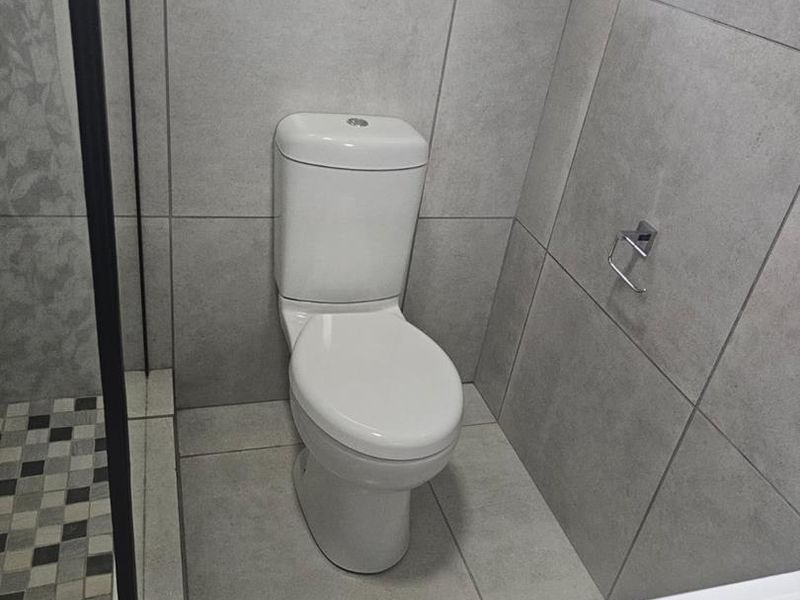 A modern bathroom featuring large format grey wall and floor tiles, a white toilet, and a glass-enclosed shower area.