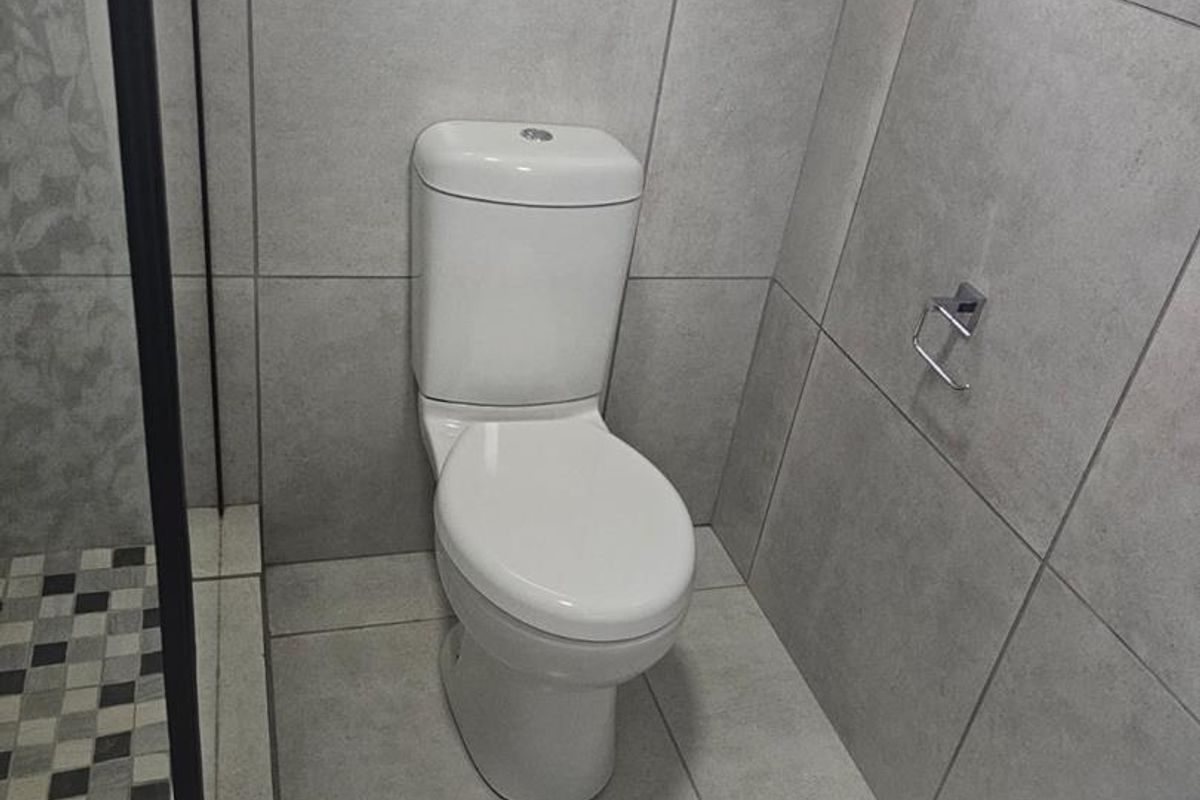 A modern bathroom featuring large format grey wall and floor tiles, a white toilet, and a glass-enclosed shower area.