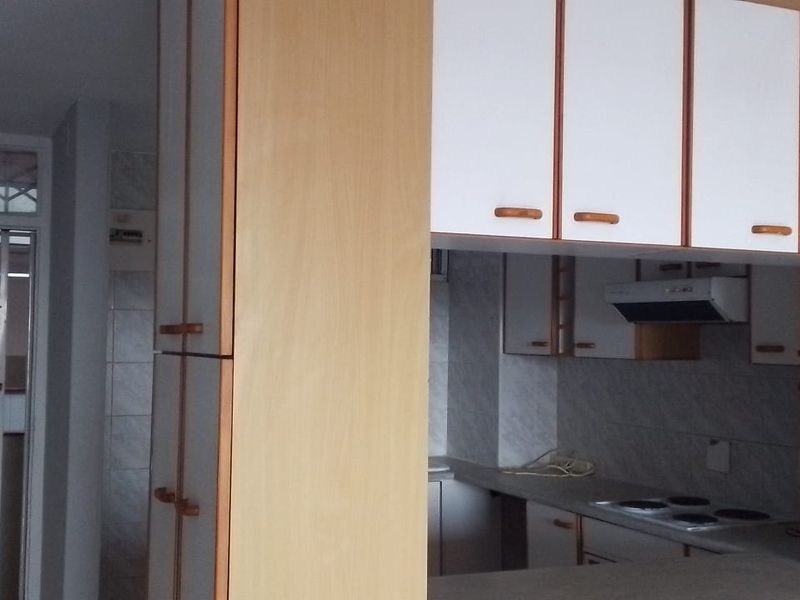 A functional kitchen featuring built-in cabinetry, an electric hob, and an extractor fan, with an adjacent security gate at the entrance.