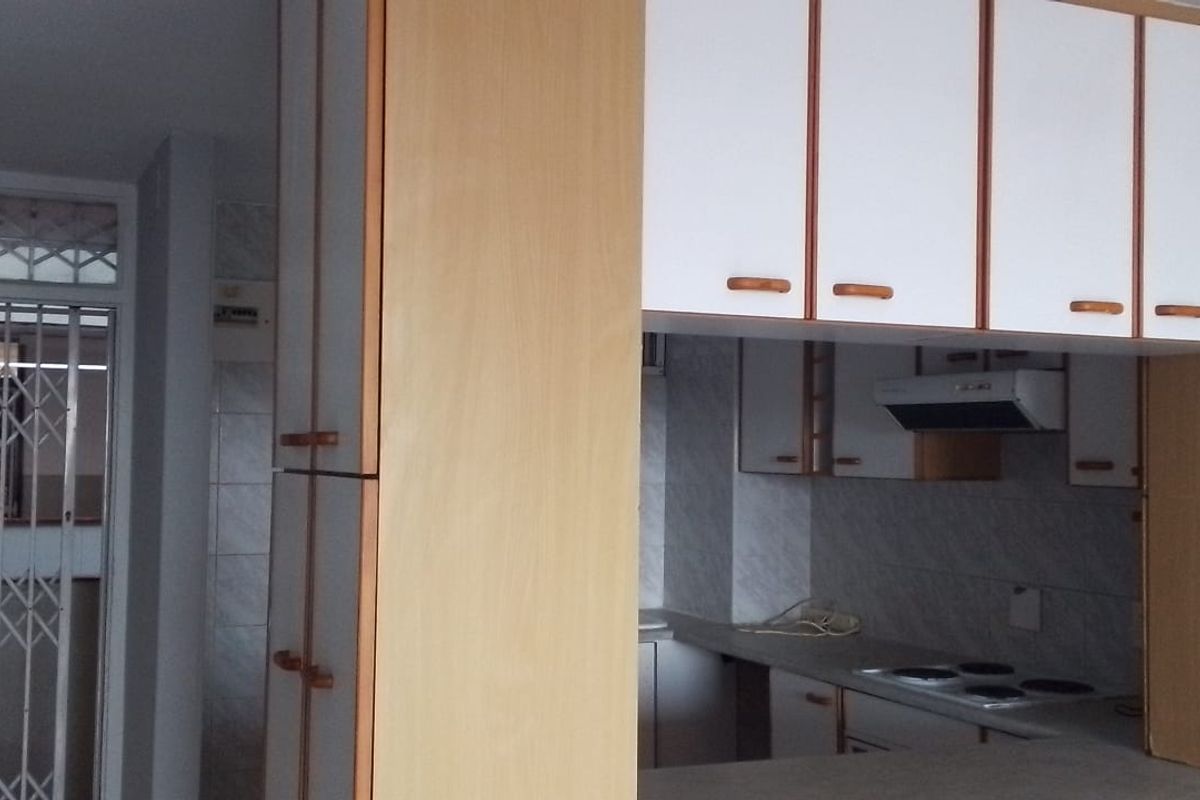 A functional kitchen featuring built-in cabinetry, an electric hob, and an extractor fan, with an adjacent security gate at the entrance.
