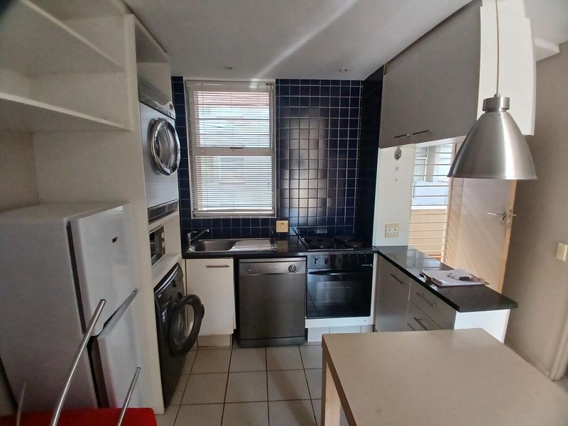 Compact kitchen featuring dark tiled backsplash, stone countertops, built-in oven, hob, and integrated laundry facilities with ample cabinetry.