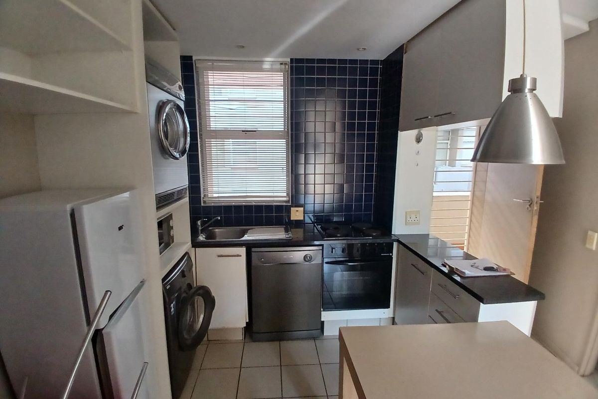 Compact kitchen featuring dark tiled backsplash, stone countertops, built-in oven, hob, and integrated laundry facilities with ample cabinetry.