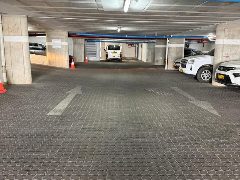 A functional underground parking garage featuring concrete structural columns, exposed utility piping, and paved flooring with directional markings.