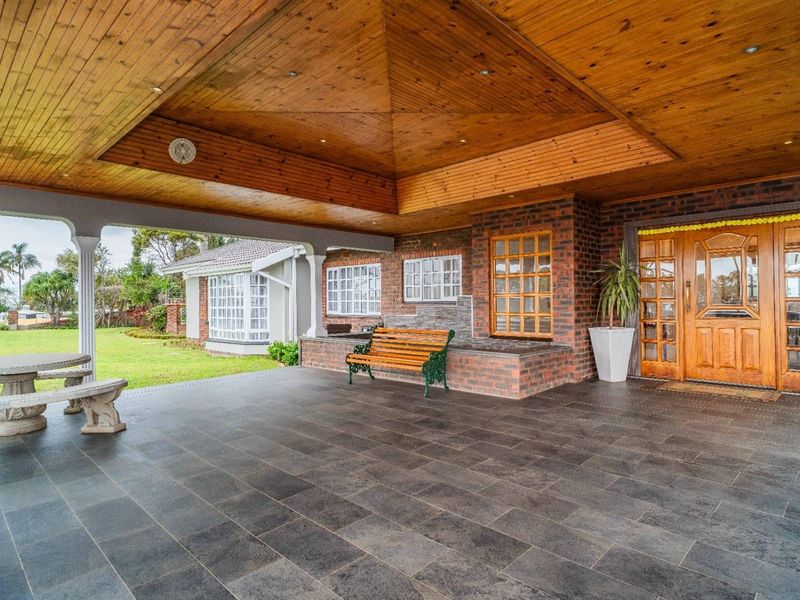 Spacious covered patio featuring a timber-clad vaulted ceiling, dark tiled flooring, and an elegant timber-framed entrance door, overlooking a well-maintained garden.