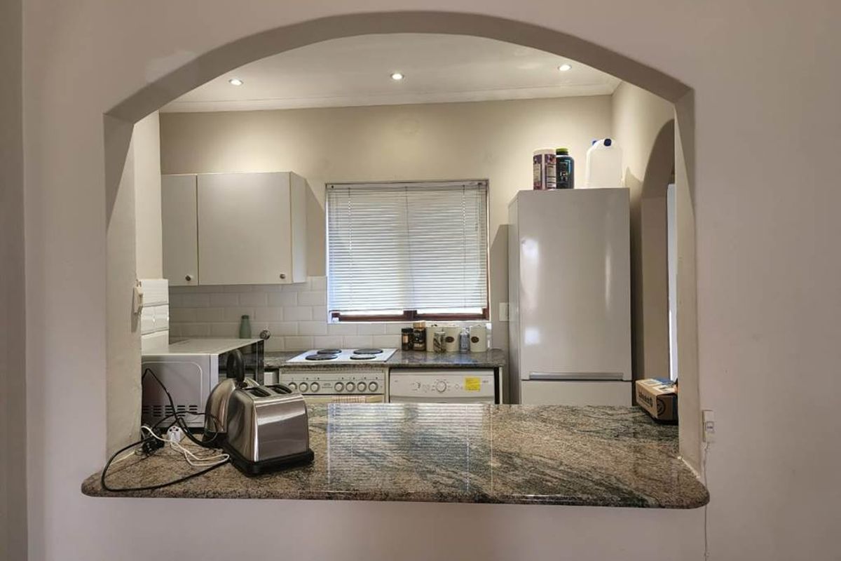 A functional kitchen featuring a granite breakfast bar, subway tile backsplash, and built-in cabinetry, viewed through a classic architectural archway.