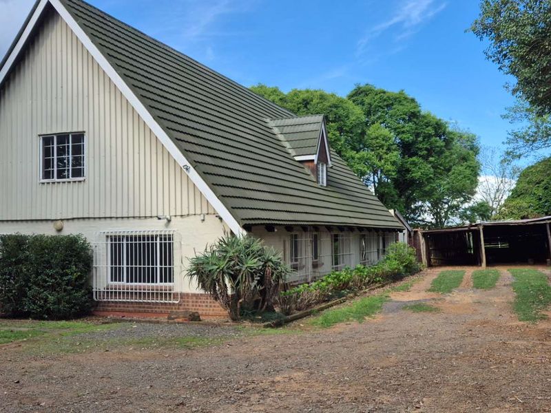 A detached house featuring a steep pitched tiled roof, timber cladding, and an attached carport, situated on a large plot with a gravel driveway.