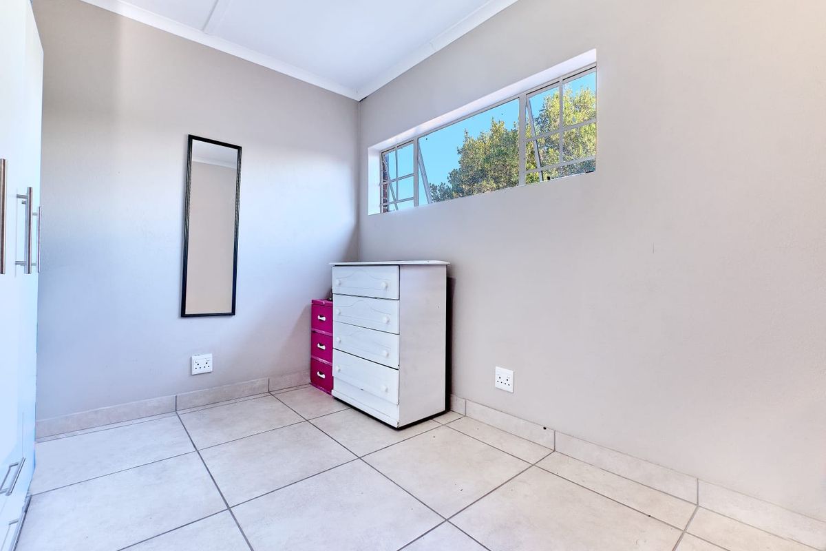 A bright bedroom featuring neutral wall tones, tiled flooring, and a high-set horizontal window providing natural light.