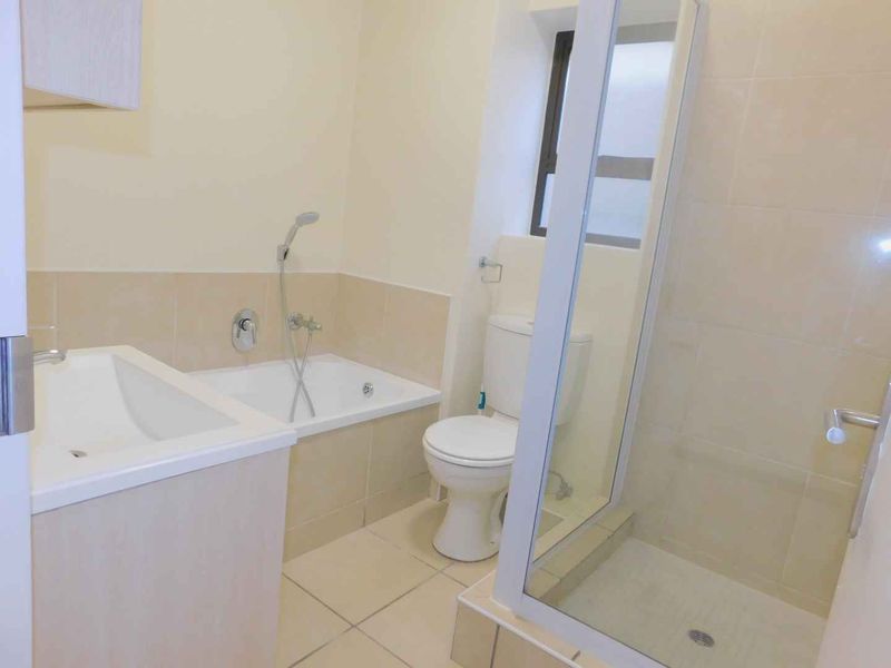 A clean, functional bathroom featuring a built-in bathtub, separate shower enclosure, toilet, and vanity cabinet with neutral wall and floor tiling.