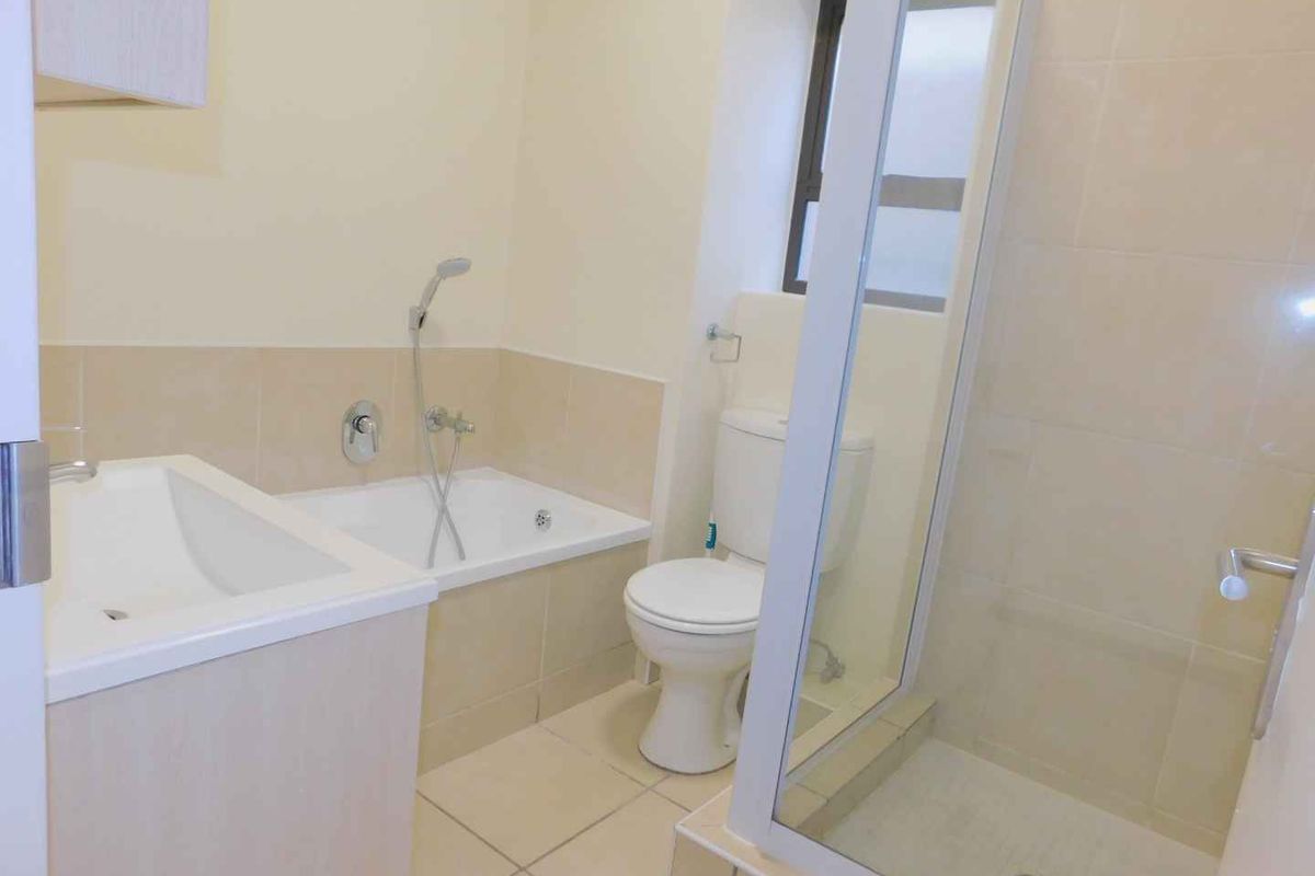 A clean, functional bathroom featuring a built-in bathtub, separate shower enclosure, toilet, and vanity cabinet with neutral wall and floor tiling.