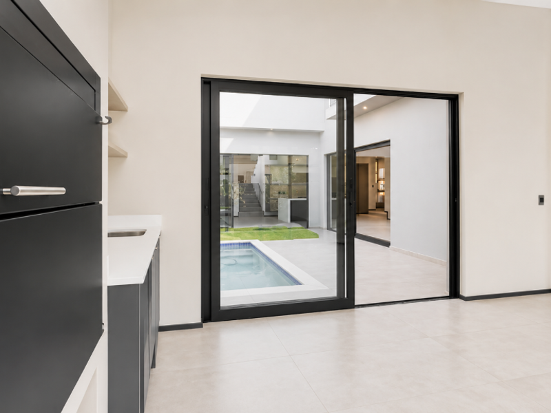 Modern open-plan living area featuring a built-in braai, sleek cabinetry, and large sliding doors opening onto a central courtyard with a pool.