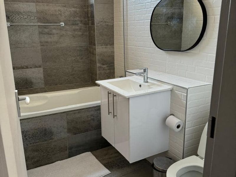 Modern bathroom featuring a bathtub with shower mixer, wall-mounted vanity with basin, toilet, and contemporary grey and white tiled finishes.