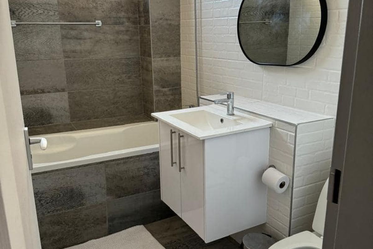 Modern bathroom featuring a bathtub with shower mixer, wall-mounted vanity with basin, toilet, and contemporary grey and white tiled finishes.
