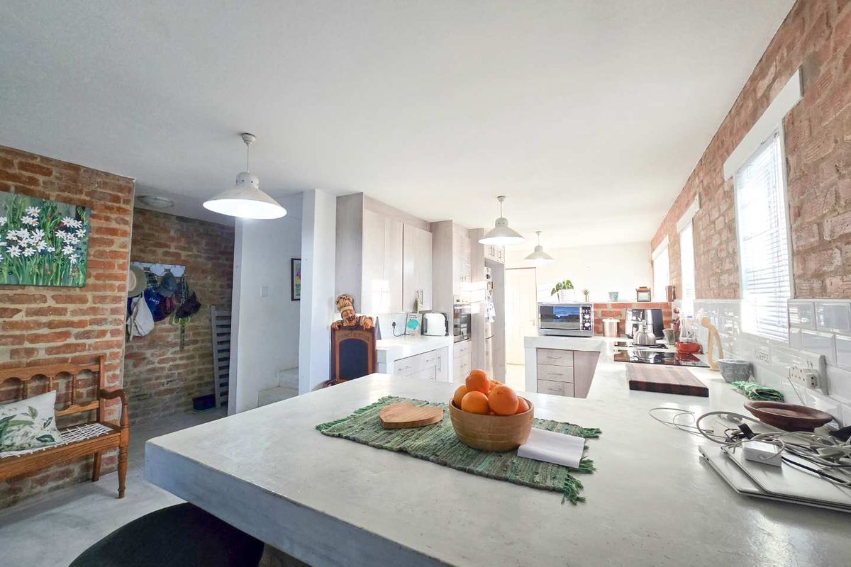 Spacious kitchen featuring exposed brick walls, a large concrete breakfast bar, modern cabinetry, and integrated appliances with ample natural light.