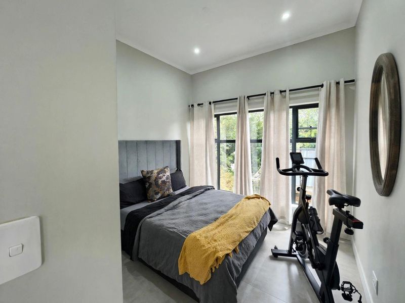 A well-lit bedroom featuring large windows, neutral wall tones, and tiled flooring, offering a clean and modern living space.