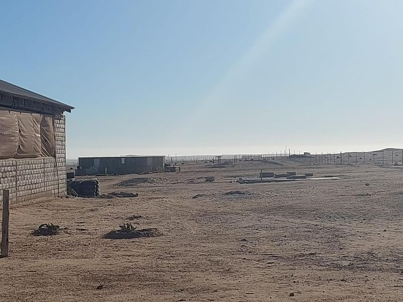 Expansive small holding land featuring a large concrete block structure with metal roofing and perimeter fencing in a rural, arid setting.