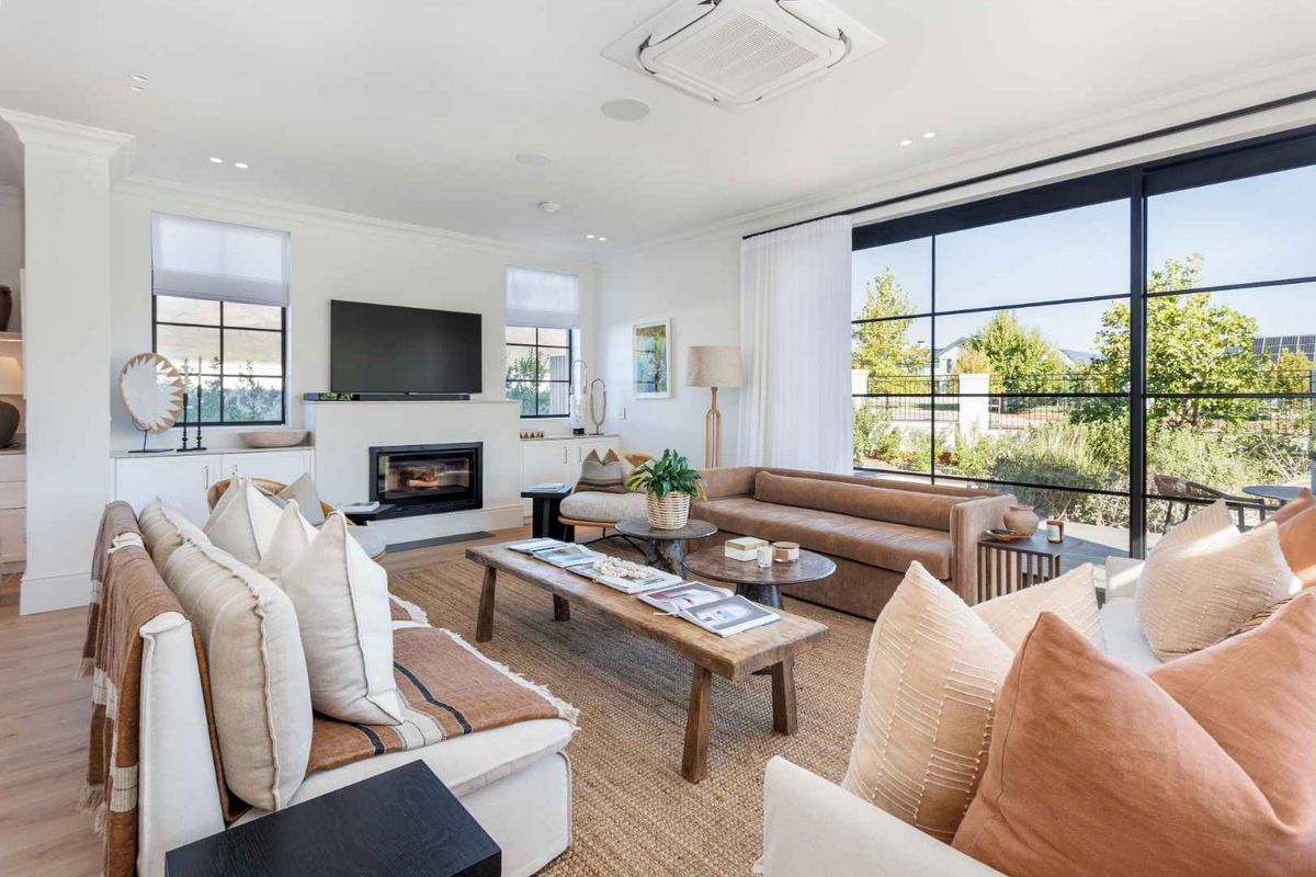 Spacious living room featuring a modern built-in fireplace, large black-framed windows, and recessed ceiling air conditioning unit.