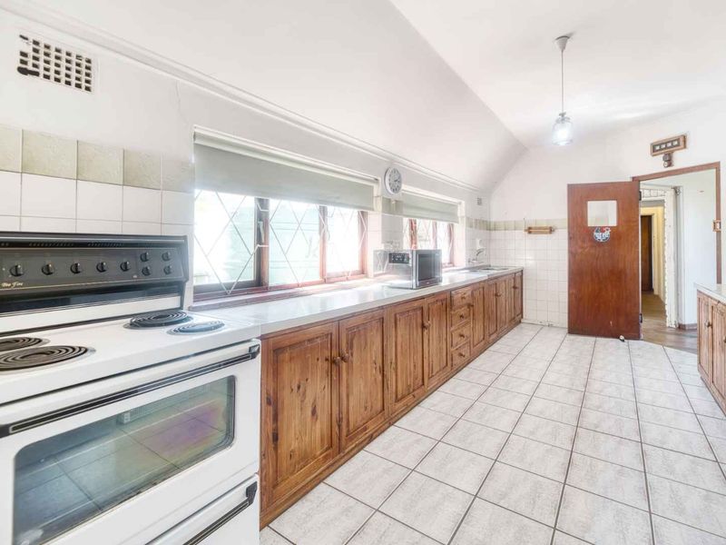 A dated kitchen featuring wooden cabinetry, tiled flooring, and a freestanding stove, offering significant potential for a modern renovation.