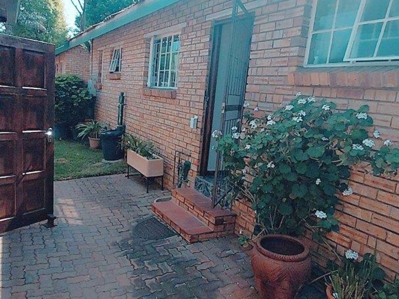 A rear exterior view of a brick cluster home featuring a paved patio area, security gate, and window bars.