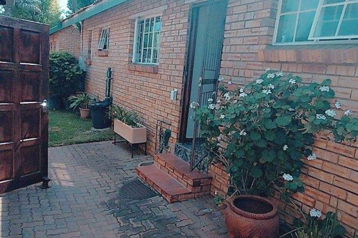 A rear exterior view of a brick cluster home featuring a paved patio area, security gate, and window bars.