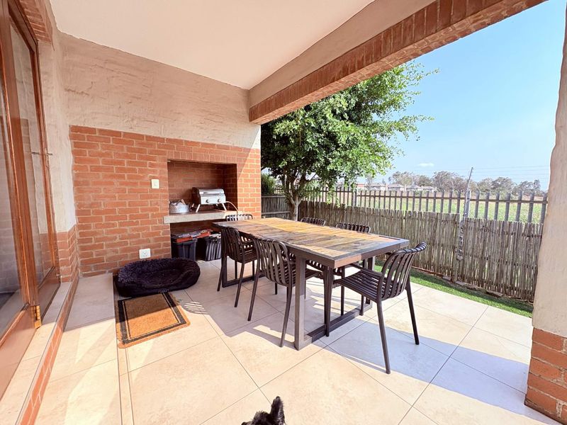 Covered patio area featuring a built-in braai, tiled flooring, and an exposed brick feature wall, overlooking a private garden space.