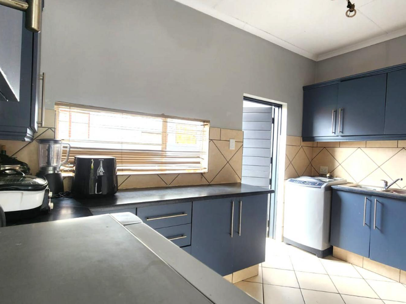 Functional kitchen featuring dark blue cabinetry, tiled backsplash, laminate countertops, and tiled flooring with direct access to an exterior door.