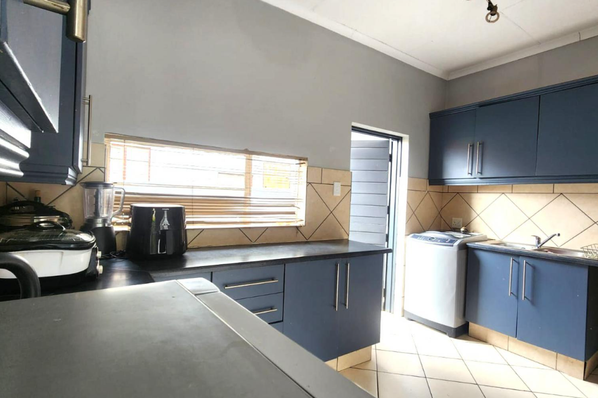 Functional kitchen featuring dark blue cabinetry, tiled backsplash, laminate countertops, and tiled flooring with direct access to an exterior door.