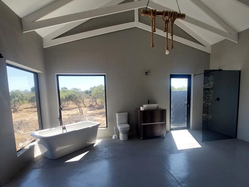 Spacious modern bathroom featuring a freestanding bathtub, walk-in shower, vanity with vessel sink, and high vaulted ceilings with exposed trusses.