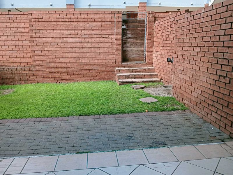 A private rear courtyard featuring a paved patio area, a small lawn, and a brick boundary wall with a gated access point.
