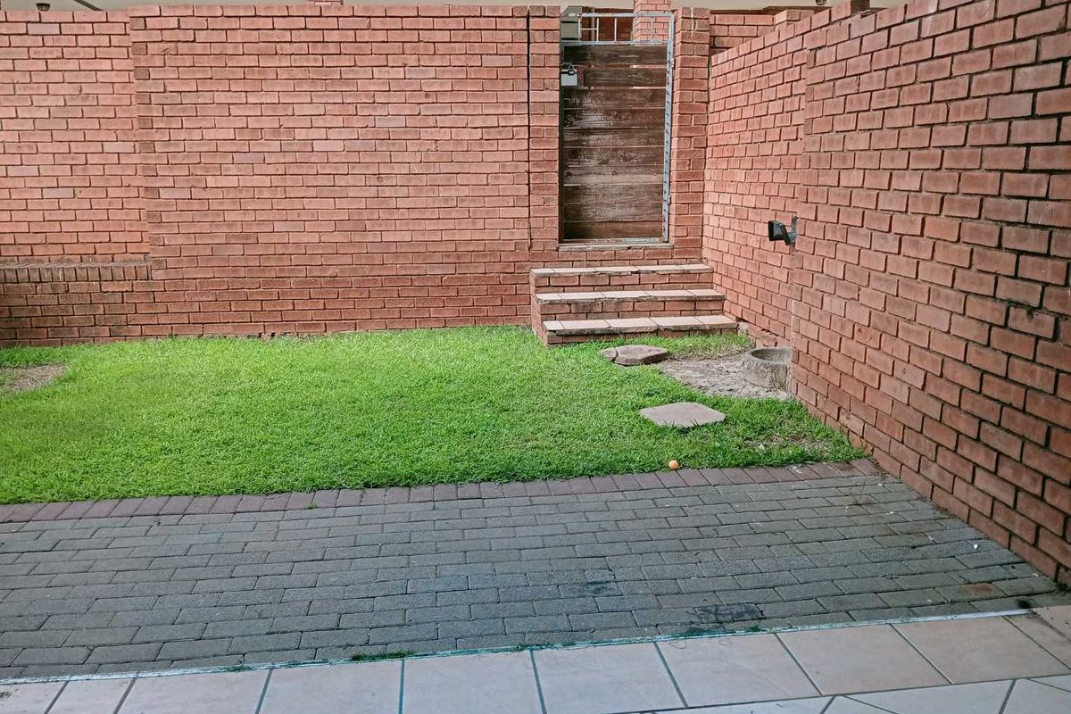 A private rear courtyard featuring a paved patio area, a small lawn, and a brick boundary wall with a gated access point.