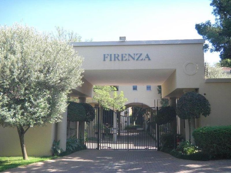 The entrance to the Firenza complex features a secure gated driveway with an architectural archway and established landscaped surroundings.