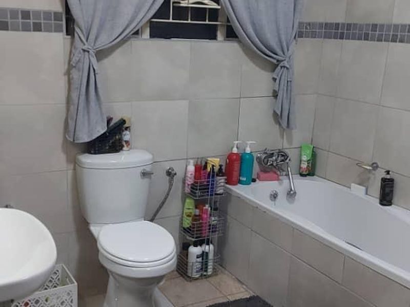 A functional bathroom featuring neutral ceramic wall and floor tiles, a built-in bathtub, a standard toilet, and a basin with chrome fixtures.