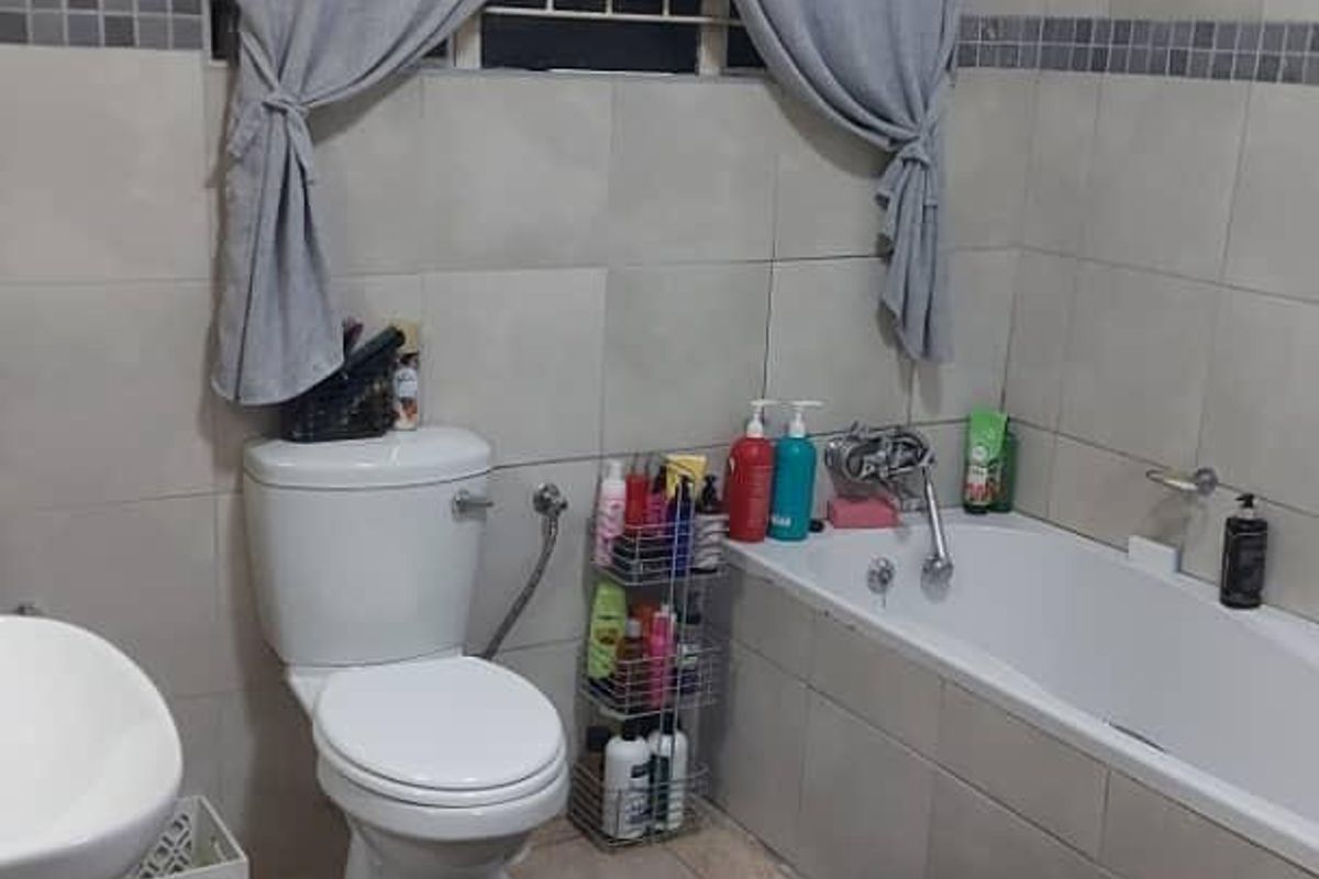 A functional bathroom featuring neutral ceramic wall and floor tiles, a built-in bathtub, a standard toilet, and a basin with chrome fixtures.