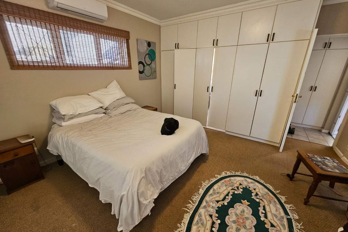 A bedroom featuring wall-to-wall built-in cupboards, carpeted flooring, and a wall-mounted split-system air conditioning unit.