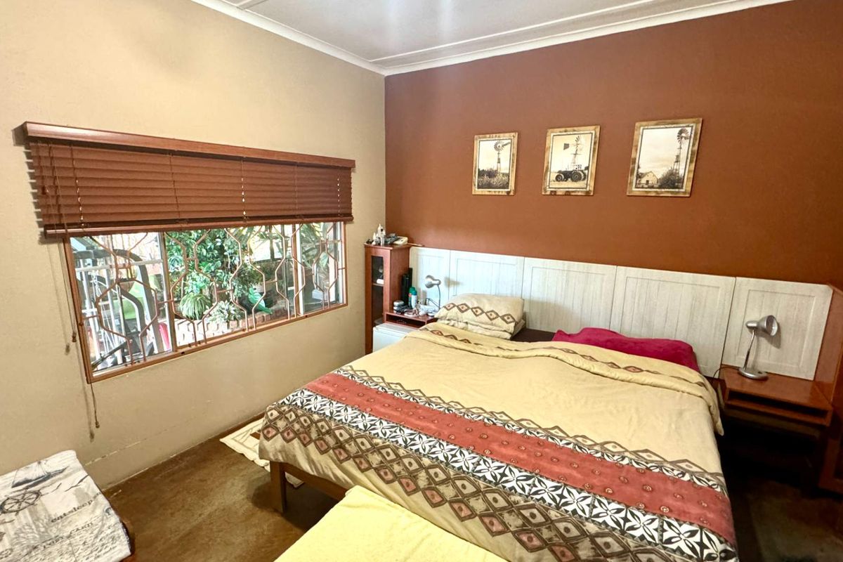A bedroom featuring a built-in headboard, horizontal window blinds, and security bars on the window.