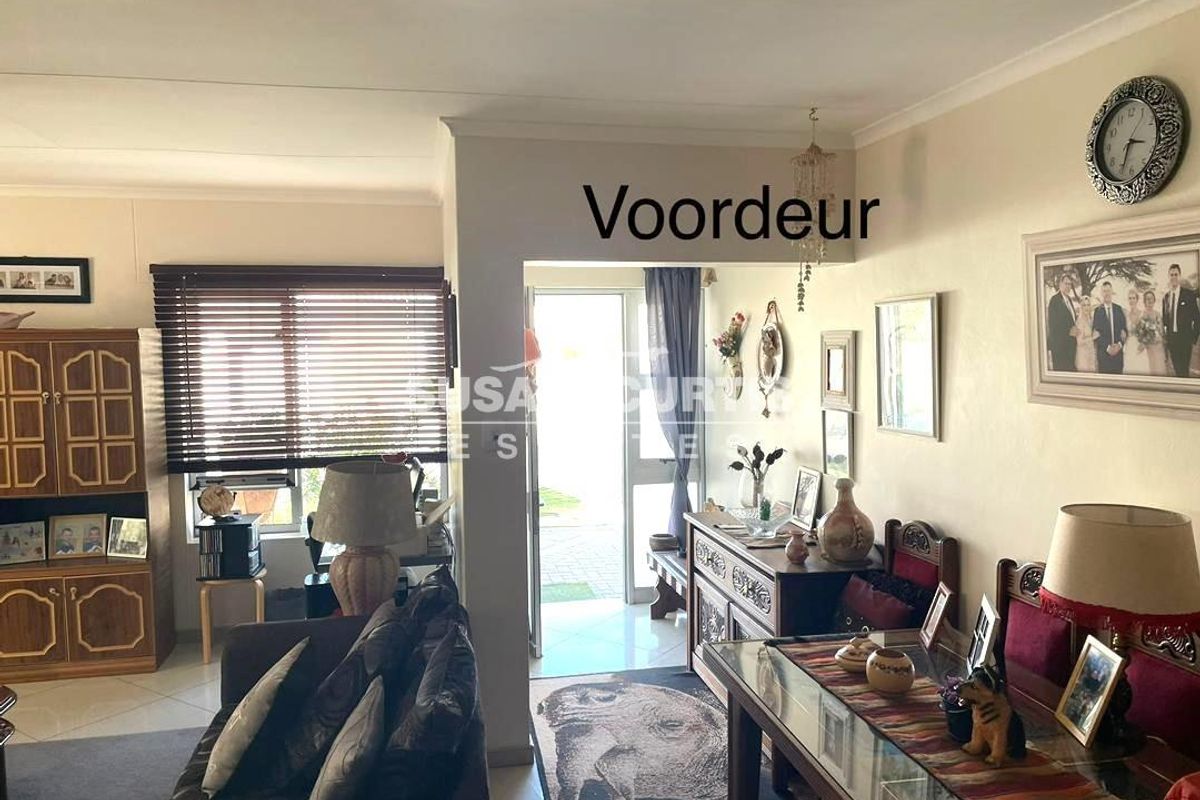 A living room area featuring tiled flooring and venetian blinds, with direct access to the front entrance.