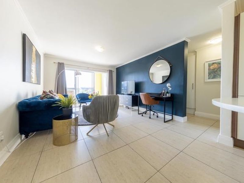 Bright open-plan living area featuring large format floor tiles, a striking dark blue accent wall, and sliding door access to an outdoor space.