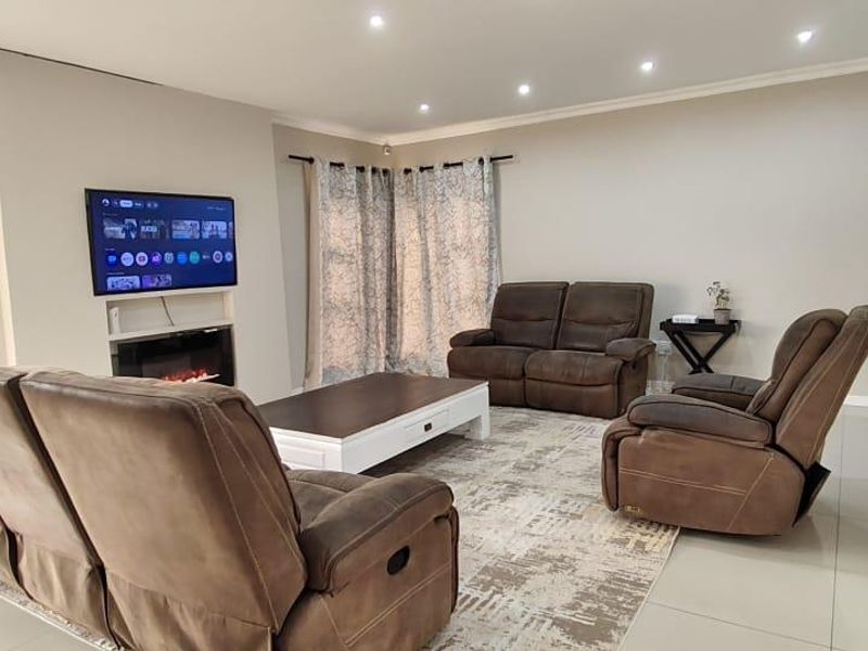 A well-maintained living room featuring tiled flooring, recessed downlighting, and a built-in electric fireplace with a wall-mounted television.