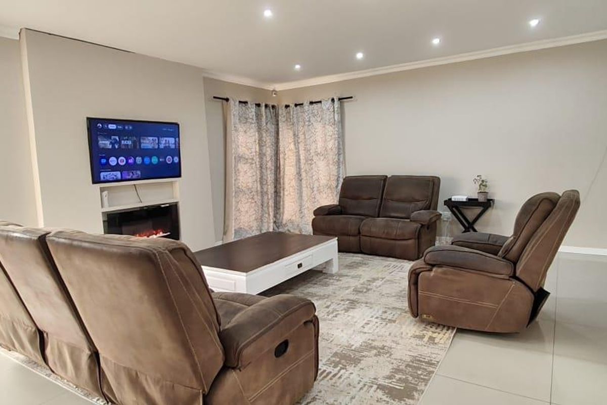 A well-maintained living room featuring tiled flooring, recessed downlighting, and a built-in electric fireplace with a wall-mounted television.
