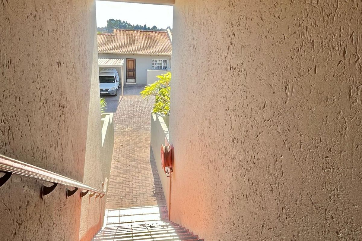 View looking down an external staircase towards a paved courtyard and driveway area with a carport.