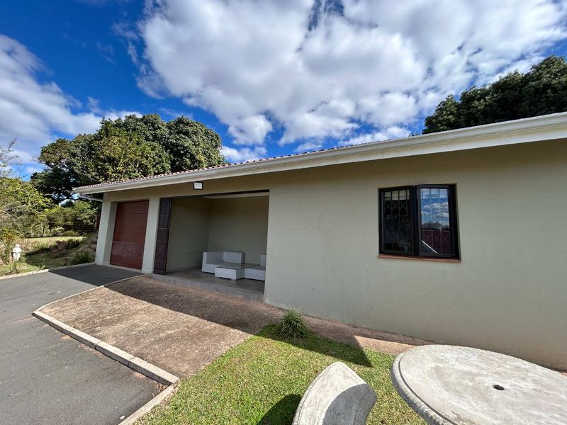 Rear exterior view of the cottage featuring a garage, covered patio area, and paved driveway with established garden surroundings.