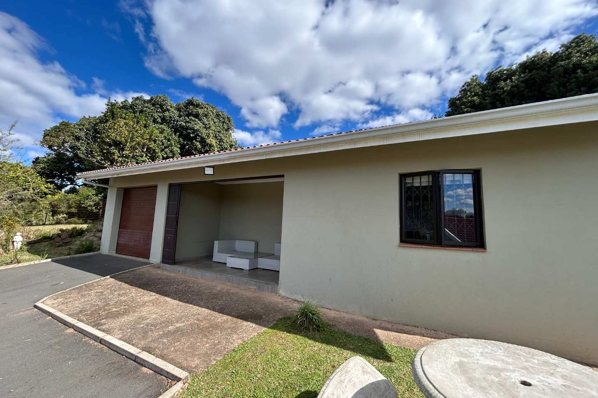 Rear exterior view of the cottage featuring a garage, covered patio area, and paved driveway with established garden surroundings.