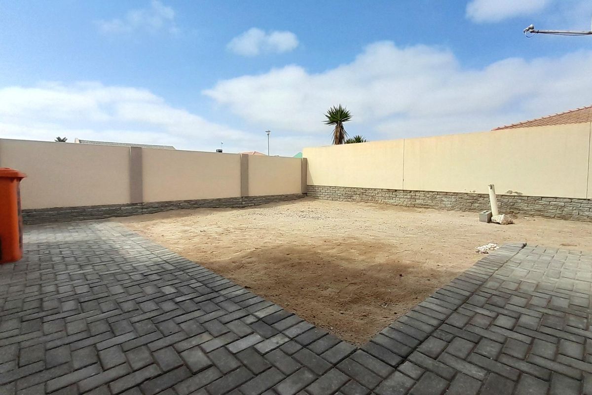 A rear courtyard featuring a paved patio area and a perimeter boundary wall with stone cladding, currently awaiting landscaping.