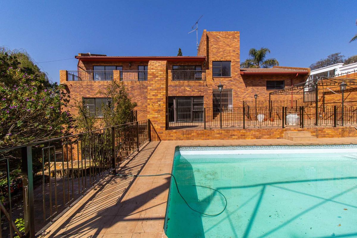 Rear view of a multi-story brick house featuring a swimming pool, paved patio area, and metal balcony railings.