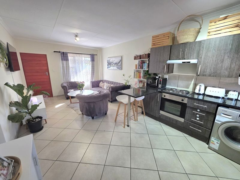 Open-plan living area featuring a modern kitchen with dark cabinetry, granite countertops, built-in oven and hob, and tiled flooring throughout.