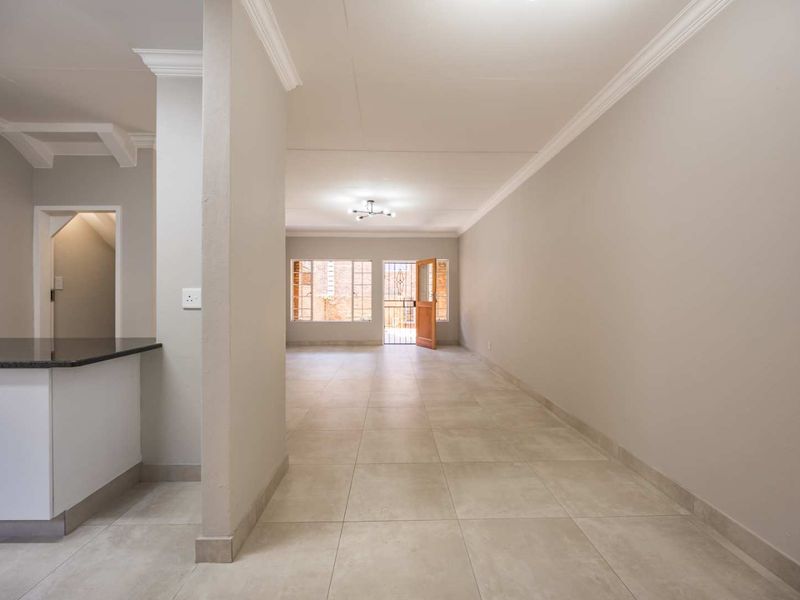 Spacious open-plan living area featuring neutral tiled flooring, modern cornicing, and direct access to the exterior through a secure entrance.