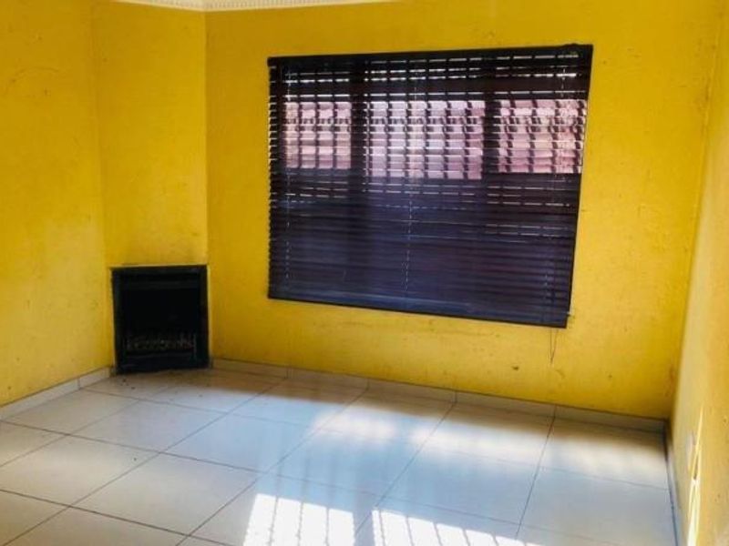 An empty living room featuring tiled flooring, a built-in fireplace, and dark venetian blinds, requiring cosmetic updates to the wall finishes.
